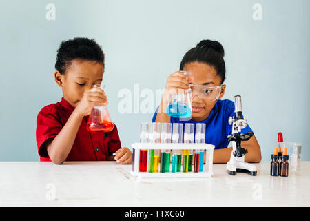 African American curioso abbastanza intelligente i bambini seduti con palloni, bicchieri e microscopio nella scuola laboratorio di chimica e di sperimentazione Foto Stock