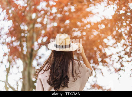 Giovane donna con cappello godendo di autunno nella foresta con la luce del sole. Viaggiare in autunno Foto Stock