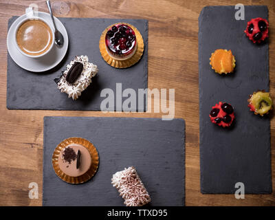 Vista dall'alto di deliziose torte di diversi sapori e colori sopra un tavolo di legno. Gustosi dessert. Dolci freschi. Una deliziosa tazza di caffè. Budino di diverse torte. Foto Stock