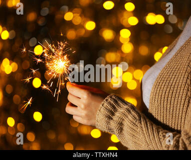 Donna che mantiene sparkler contro defocalizzata luci, close up Foto Stock