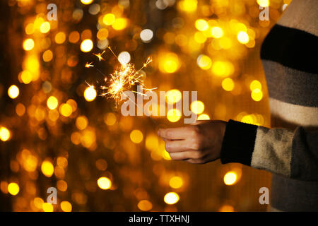 Donna che mantiene sparkler contro defocalizzata luci, close up Foto Stock