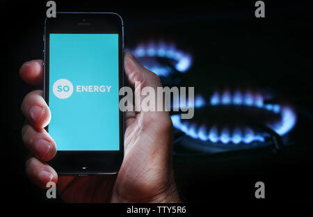 Un uomo che guarda il logo del sito web per la società energetica così l'energia sul suo telefono cellulare nella parte anteriore della sua cucina a gas (solo uso editoriale) Foto Stock