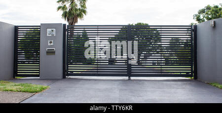 Viale di metallo proprietà cancelli di ingresso impostato nel recinto di cemento con giardino di alberi in background Foto Stock