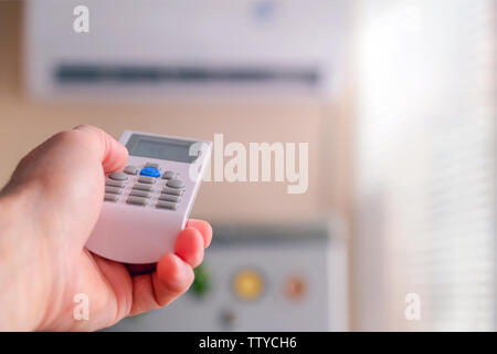 Mano maschio con il condizionatore d'aria di controllo remoto. L'uomo gli interruttori modalità di climatizzazione. Regola la temperatura di raffreddamento della camera. Foto Stock