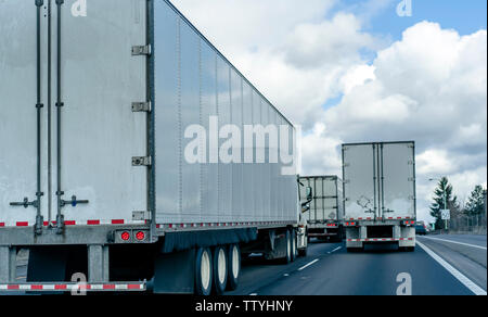 Vista posteriore del convoglio di industriale di trasporto merci di big rig semi carrelli con semirimorchi in esecuzione sulla larga strada statale su diverse linee fo Foto Stock