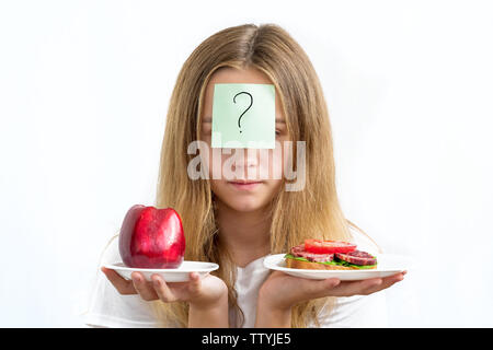 Ritratto di giovane bella ragazza in una camicia bianca, tenendo una salsiccia panino e mela rossa nelle mani di pesatura con un punto interrogativo sul per Foto Stock