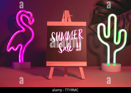 Estate vendita sulla lavagna con flamingo e cactus neon pink e la luce blu sulla tavola.mock up modello per aggiunta di testo Foto Stock