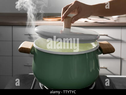 Femmina di mano che tiene il coperchio sopra la padella in cucina Foto Stock