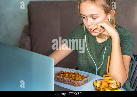 Ragazza lavora a un computer e si mangia il fast food. Cibo malsano: chips, cracker, candy, waffle, cola. Il cibo spazzatura, concetto. Foto Stock