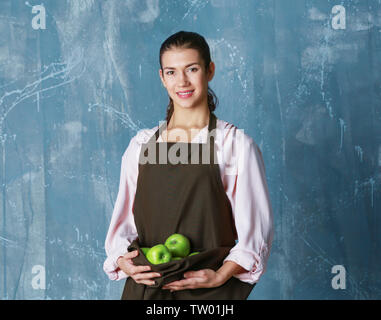 Donna che mantiene le mele nel grembiule sul colore di sfondo Foto Stock