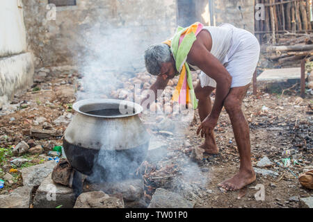 Un uomo di riscaldamento acqua su un fuoco aperto per un bagno mattutino in India del sud. Foto Stock