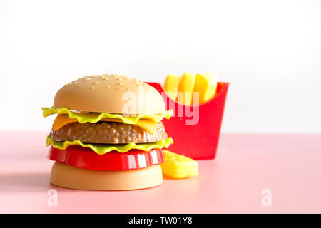 Hamburger di plastica, insalata di pomodoro, la frittura di patate con su sfondo rosa. Orientamento orizzontale. Giocattolo per bambini è. Concetto di nocivi cibi artificiali. Plas Foto Stock