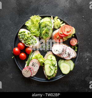 Vegano diversi panini con verdure, Rafano, sedano, pomodoro, pane di segale su sfondo nero. Top vew. Antipasto di partito. Lay piatto. Foto Stock