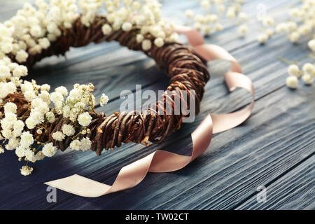 Bella ghirlanda floreale con nastro di raso scuro su sfondo di legno Foto Stock