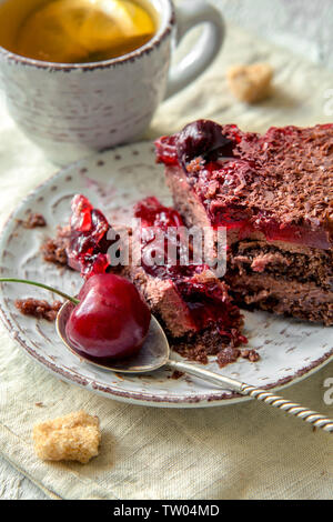 Un pezzo di torta al cioccolato con scaglie di cioccolato e frutti di bosco. Il tè con limone sul tavolo Foto Stock