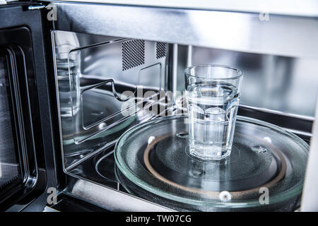 Vista interna di nuovo pulita staniless, forno a microonde con una tazza di acqua pura. Foto Stock