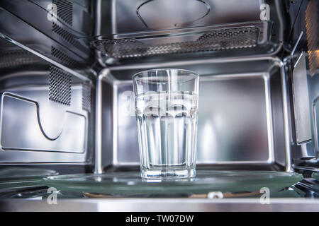 Vista interna di nuovo pulita staniless, forno a microonde con una tazza di acqua pura. Foto Stock