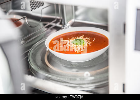 Vista interna di nuovo pulita staniless forno a microonde con una zuppa di pomodoro in piastra bianca. Foto Stock