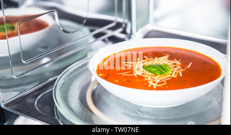 Vista interna di nuovo pulita staniless forno a microonde con una zuppa di pomodoro in piastra bianca. Foto Stock