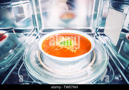 Vista interna di nuovo pulita staniless forno a microonde con una zuppa di pomodoro in piastra bianca. Foto Stock