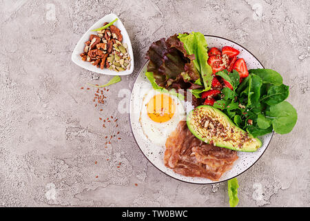 Piastra con un cheto la dieta alimentare. Uova fritte, pancetta, avocado, rucola e fragole. Cheto prima colazione. Vista superiore Foto Stock