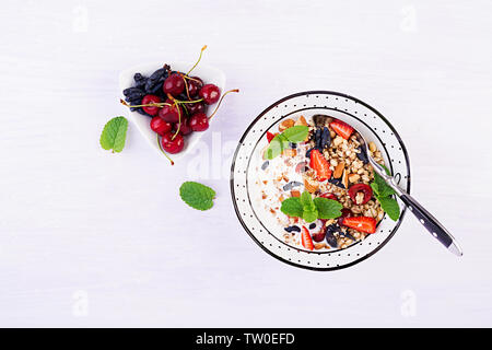 Una sana prima colazione - granola, fragole, ciliegia, caprifoglio berry, dadi e lo yogurt in una ciotola. Concetto vegetariano cibo. Vista superiore Foto Stock