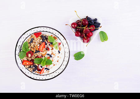 Una sana prima colazione - granola, fragole, ciliegia, caprifoglio berry, dadi e lo yogurt in una ciotola. Concetto vegetariano cibo. Vista superiore Foto Stock