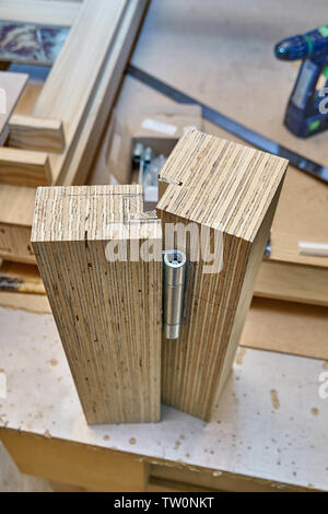 La porta di legno del processo di fabbricazione. La cerniera dello sportello a l'installazione. Macchine per la lavorazione del legno e la produzione di falegnameria. Fabbricazione di mobili. Close-up Foto Stock