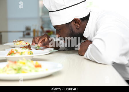 African American chef l'aggiunta di rosmarino di gustoso piatto in cucina Foto Stock