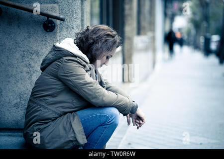 Donna attraente affetti da depressione abbattimento triste infelice heartbroken e solitaria seduta in città strada urbana in salute mentale dolore emotivo Abu Foto Stock