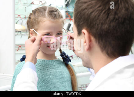 Giovane medico aiutando bambina a scegliere nuovi occhiali in negozio Foto Stock