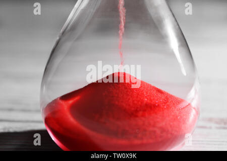 Il passare del tempo concetto. Crystal clessidra con sabbia rossa sulla luce sullo sfondo di legno Foto Stock