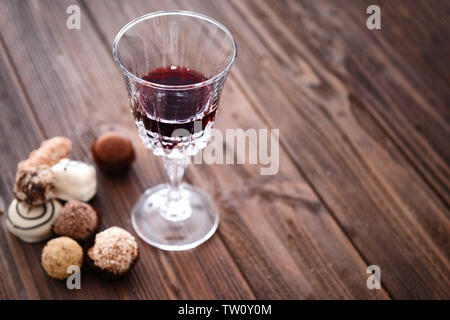 Bicchiere di vino rosso e cioccolatini su sfondo di legno Foto Stock