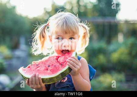 Ritratto di bella bionda bambina con due ponytails mangiando anguria. Kid mangia frutta Foto Stock