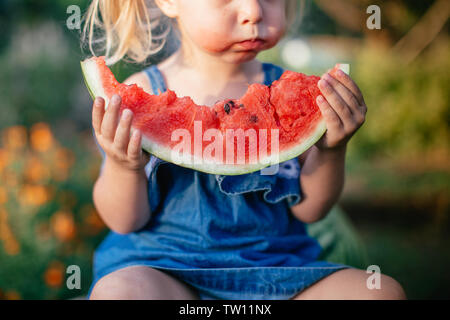 Ritratto di bella bionda bambina con due ponytails mangiando anguria. Kid mangia frutta Foto Stock