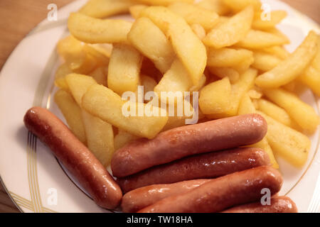 Patate fritte con salsicce fritte su una piastra da vicino Foto Stock