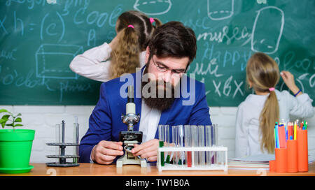 Uomo Barbuto maestro lavora con microscopio e provette per la prova in biologia classe. Spiegare la biologia per i bambini. Biologia svolge ruolo nella comprensione delle complesse forme di vita. Insegnante della Scuola di biologia. Foto Stock