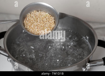 Materie riso marrone in una coppa di misurazione sulla pentola con acqua bollente Foto Stock