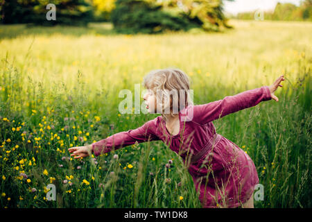 Carino in età prescolare caucasico bionda ragazza in rosso abito rosa selvatica Raccolta fiori di campo in erba alta in prato all'aperto. Bambino felice kid godendo estate al Foto Stock