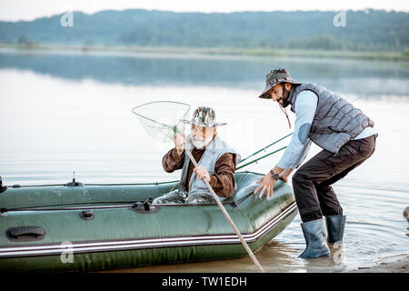 Nonno figlio con la preparazione per la pesca, spingendo fuori la barca sul lago di prima mattina Foto Stock