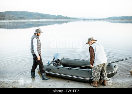 Nonno figlio con la preparazione per la pesca, spingendo fuori la barca sul lago di prima mattina Foto Stock