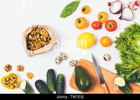 Verdure fresche e verdi accanto al pacchetto di dadi su sfondo bianco, vista dall'alto. Piano di composizione dei laici di una sana dieta variata di pomodori, noci, l Foto Stock