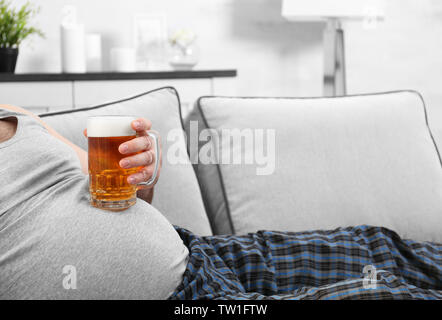 Uomo con un bicchiere di birra per la sua grande pancia a casa Foto Stock