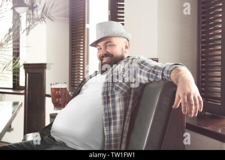 Uomo con un bicchiere di birra per la sua grande pancia in pub Foto Stock