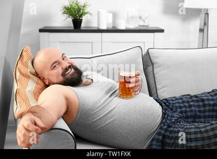 Uomo con un bicchiere di birra per la sua grande pancia a casa Foto Stock