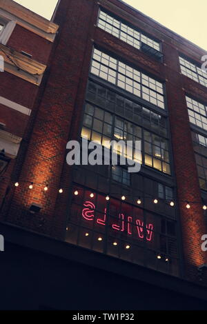 Una casa di mattoni in un stile industriale in Londra, Regno Unito. In una finestra si illumina di un colore rosa segno al neon. Davanti a questo è presente una luce stringa, che si illumina come bene. Foto Stock