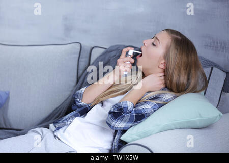 Malati giovane donna utilizzando spray gola a casa Foto Stock