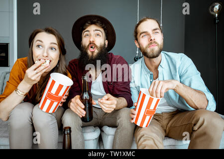 Giovani amici la visione di alcuni film, seduti insieme con pop cornes sul lettino a casa Foto Stock