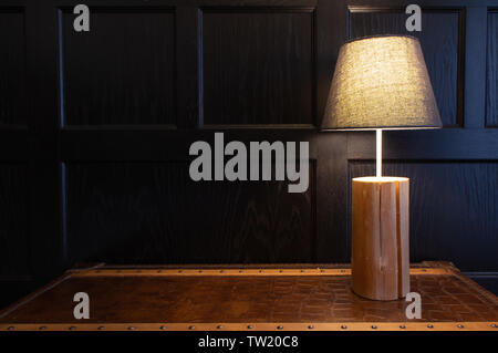 Lampada singola su un tavolo di fronte a cassettoni scuro muro con spazio di copia Foto Stock