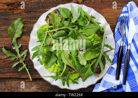 Mescolare le foglie fresche di spinaci della Nuova Zelanda, rucola, lattuga, , barbabietole da insalata in legno scuro dello sfondo. Vista superiore . Foto Stock